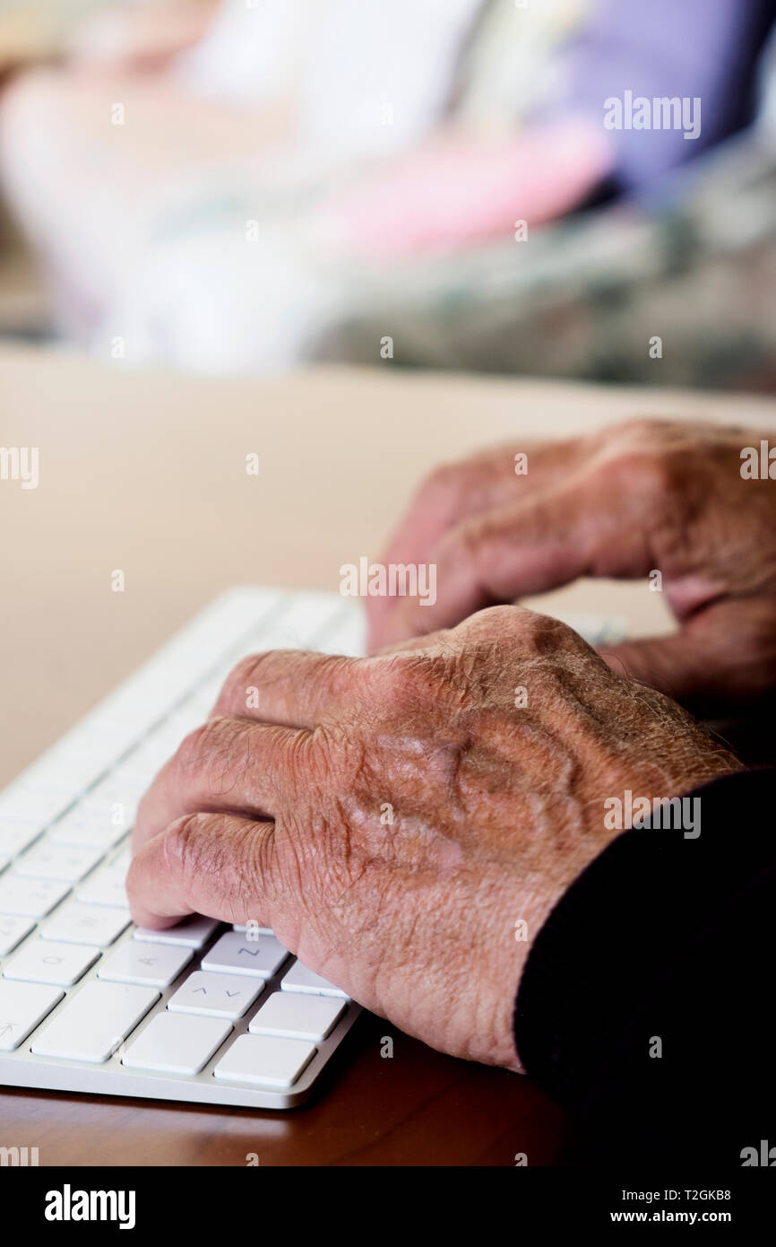 Primo piano di un vecchio uomo caucasico seduta in un elegante tavolo in legno digitando una tastiera Foto Stock