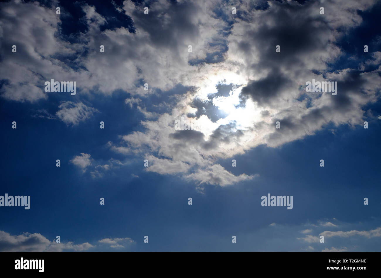 Sole brillante dietro le nuvole nel cielo blu sullo sfondo Foto Stock