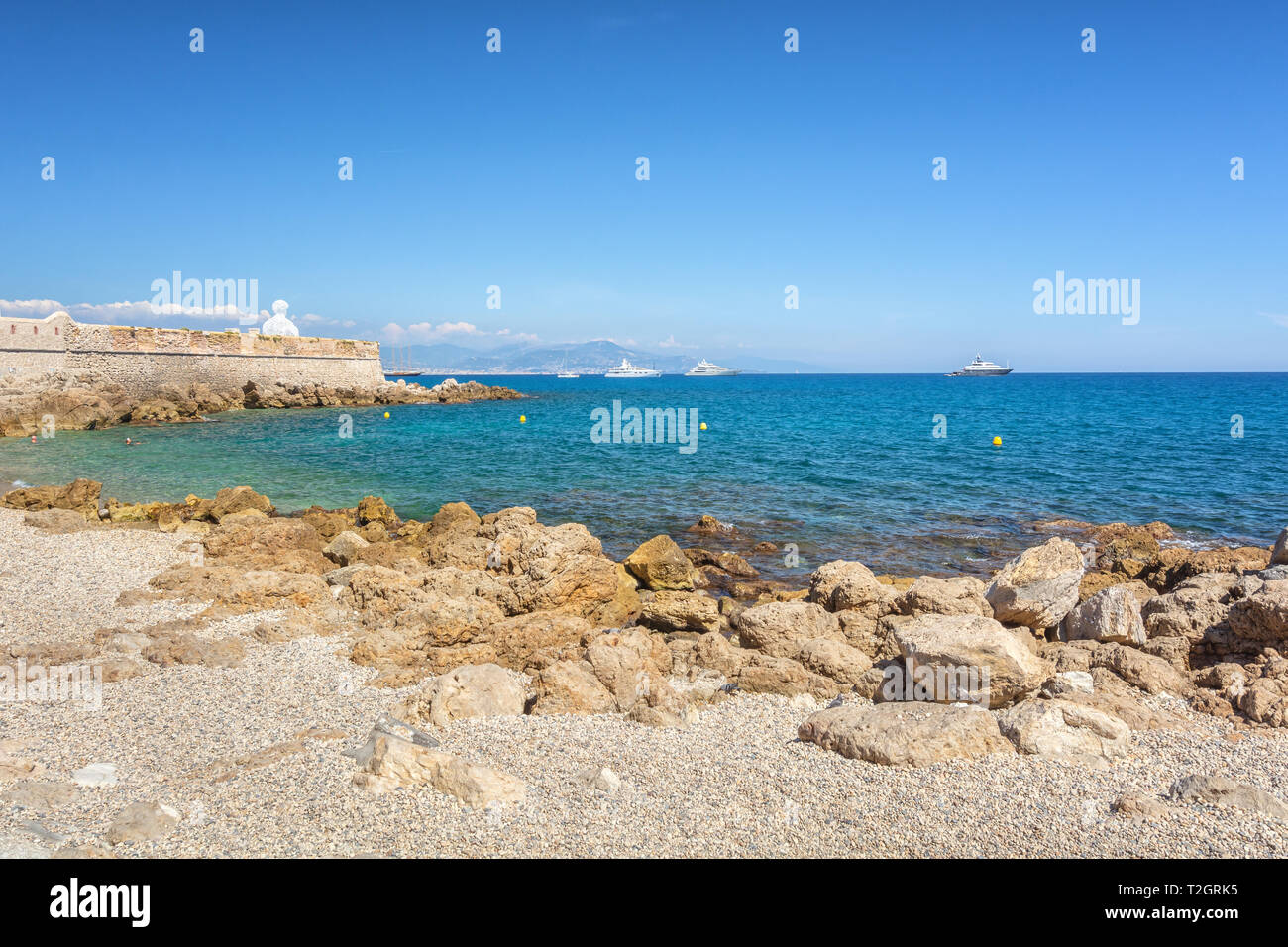 Le vecchie mura della città lungo la costa della cittadina francese di Antibes con sopra la testa delle famose opere d'arte nomade Foto Stock