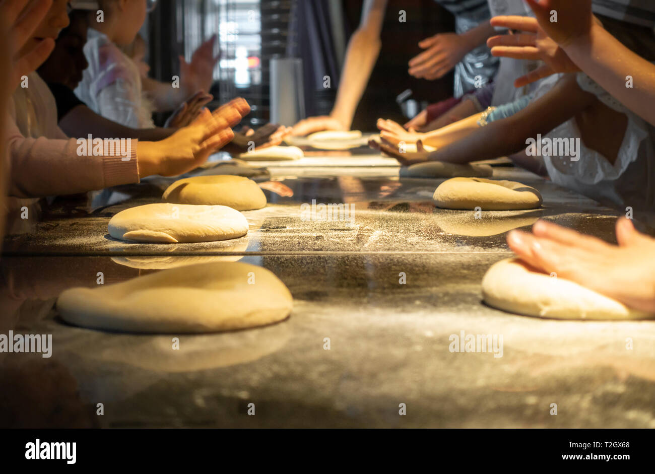 Un gruppo di bambini per impastare la pasta della pizza in una pizza facendo festa di compleanno. Giovani mani premere e impastare la pasta su un tavolo ricoperto con farina. Foto Stock