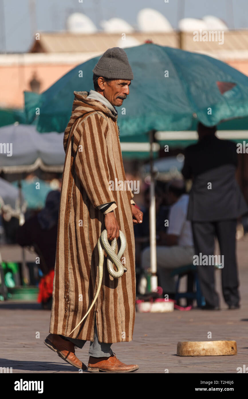 Un uomo marocchino nativo, incantatore di serpenti, cammina per strada con serpente avvolto in mano al mercato Foto Stock