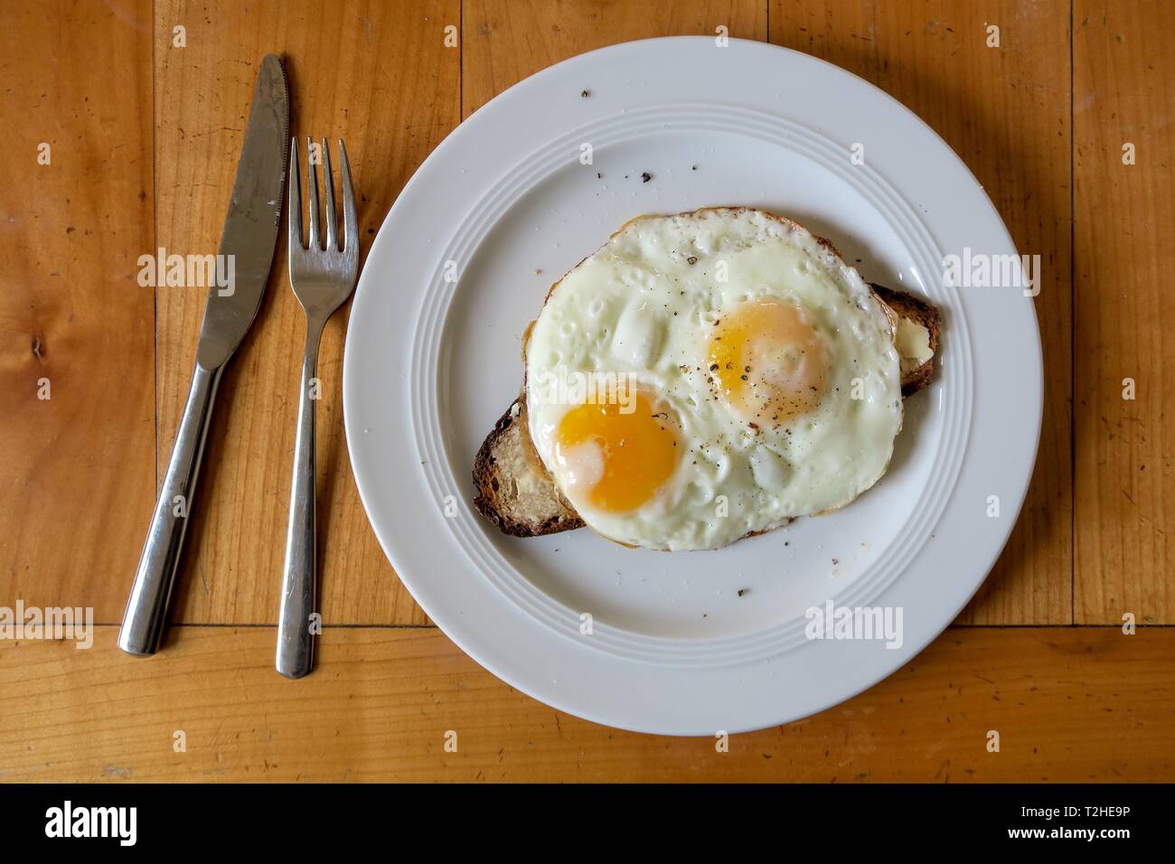 Strammer Max, due uova fritte sul pane, piastra bianca, tavolo in legno, posate coltello e forchetta, cucina casalinga, cucina tedesca, Germania Foto Stock