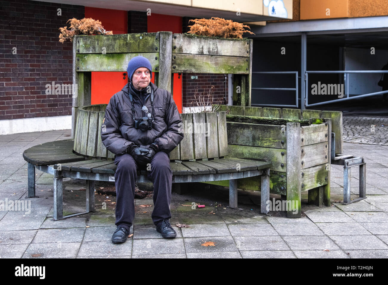 Uomo anziano con fotocamera poggia su una panca in Moabit di Berlino. Rustico panca in legno con vasi per piante Foto Stock