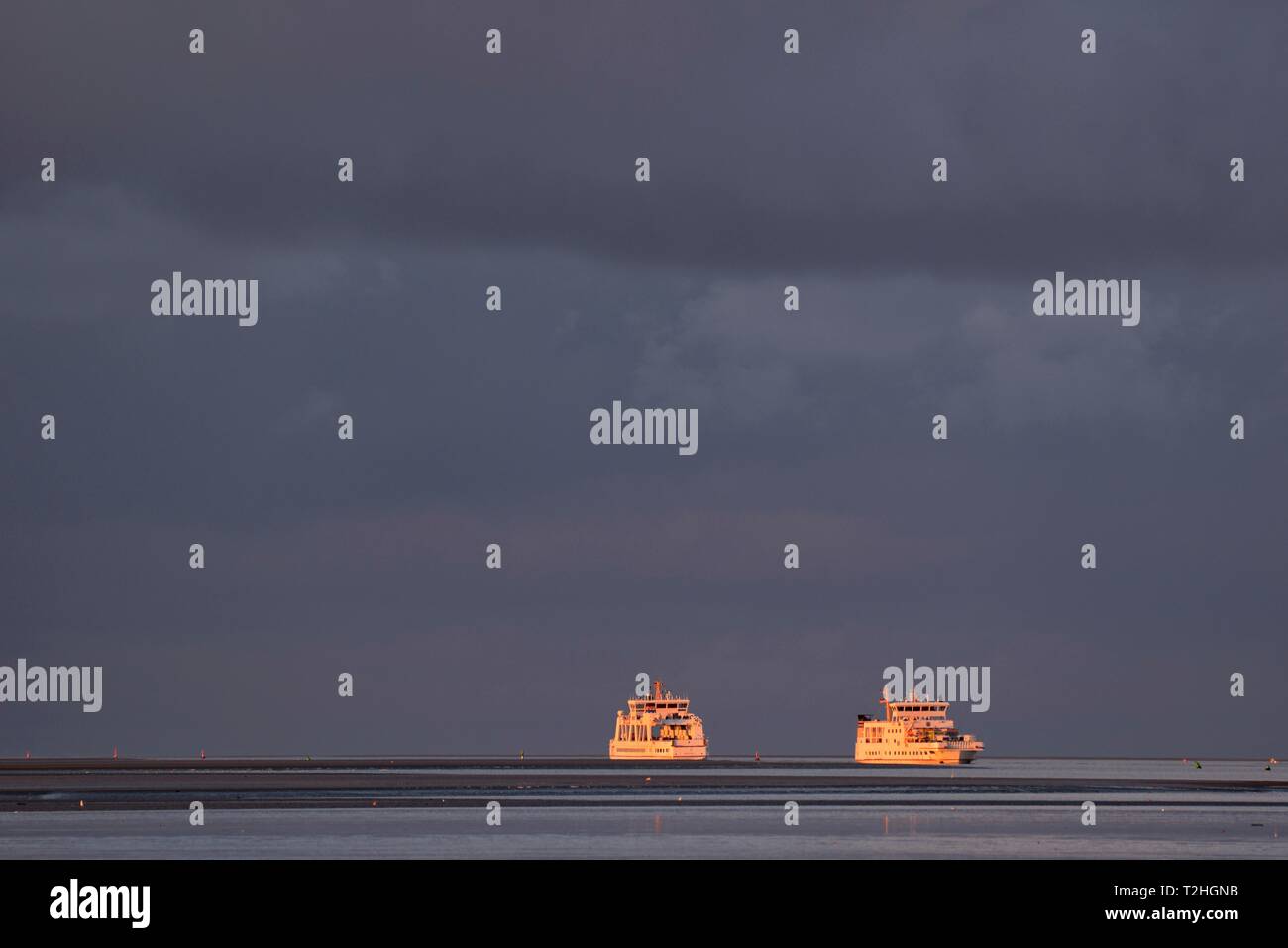 Due traghetti di soddisfare in via navigabile di Norderney nella luce della sera con nuvole scure, Mare del Nord, Bassa Sassonia, Germania Foto Stock