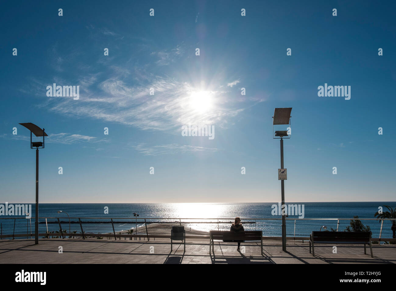 La donna si siede su un banco di lavoro godendo il forte sole invernale sul Mediterraneo presso il Mirador de la Plaza de Topete, città di Alicante, Spagna Foto Stock