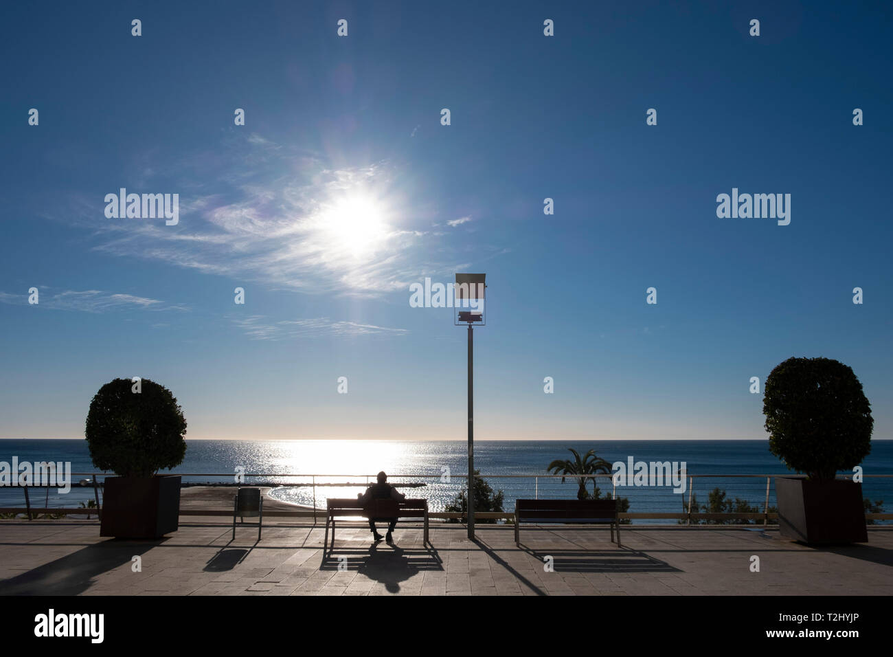Uomo si siede su un banco di lavoro godendo il forte sole invernale sul Mediterraneo presso il Mirador de la Plaza de Topete, città di Alicante, Spagna Foto Stock