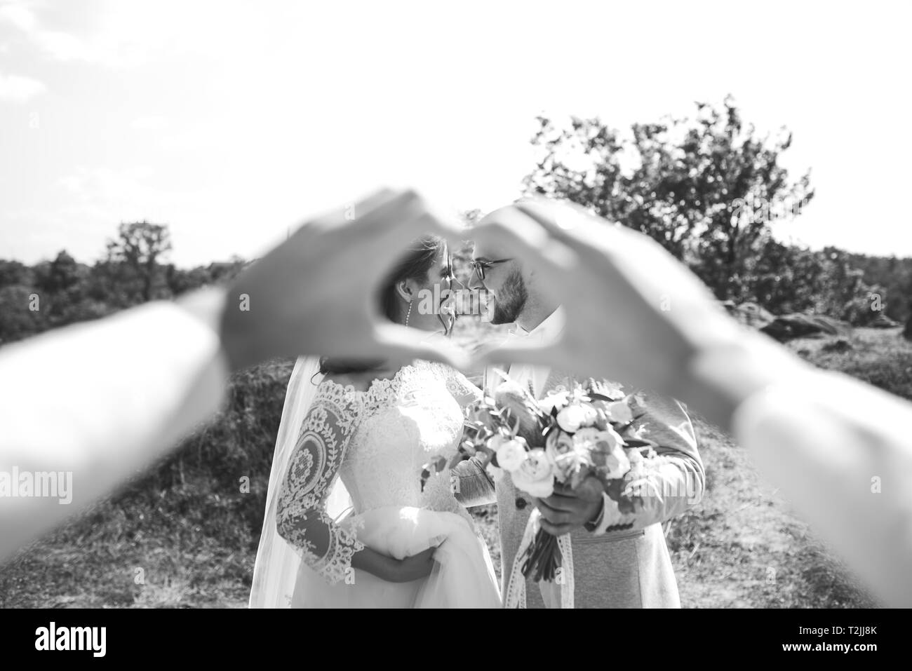 Mani piegate a forma di cuore in cui si può vedere il barbuto lo sposo con gli occhiali in una giacca grigia e sposa. Foto Stock