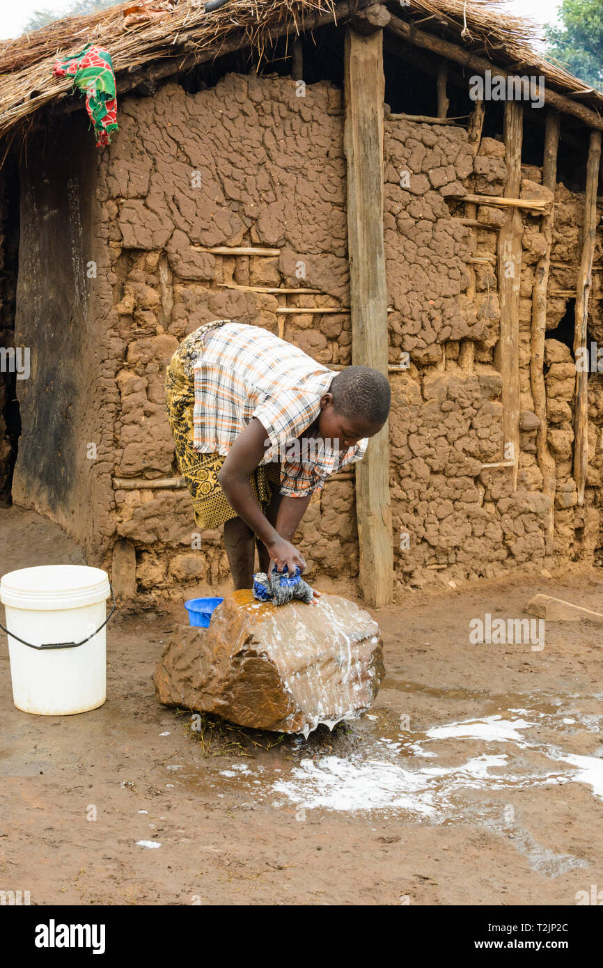 Malawiani ragazza lava vestiti su una pietra davanti a una capanna di fango in un villaggio Foto Stock