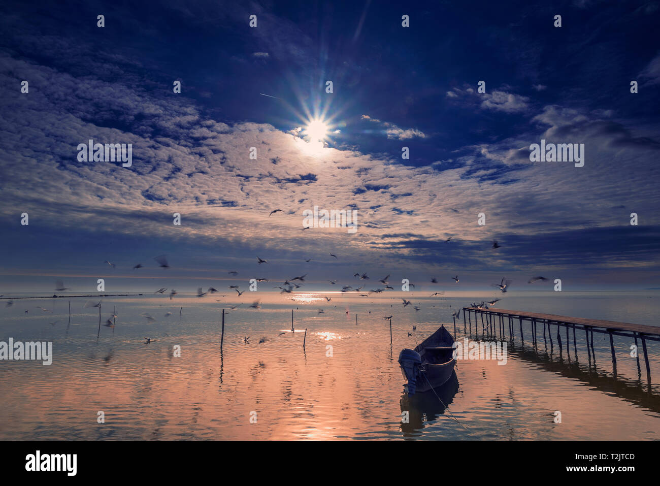 Il lago di scena al mattino all'alba con gli uccelli che volano sopra il lago e una barca e un pontone in primo piano con un sole luminoso sulla copia sky shot in Foto Stock