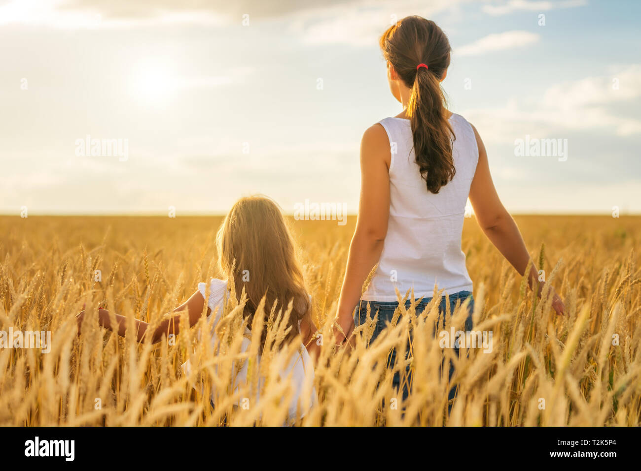 Giovane donna e sua figlia camminando sul golden campo di grano a sunny serata d'estate. Foto Stock