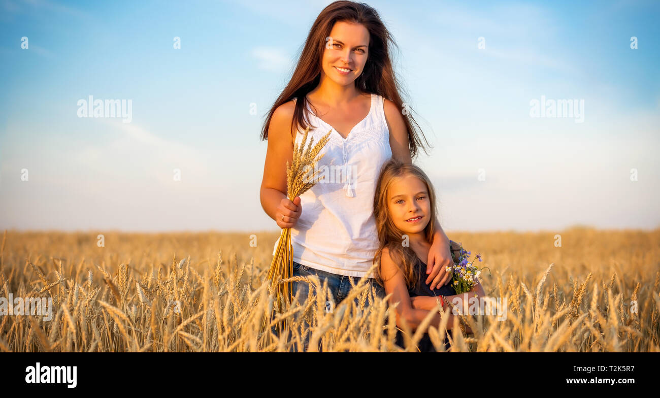 Giovane madre e figlia in piedi sul campo di grano alla sera d'estate. Foto Stock