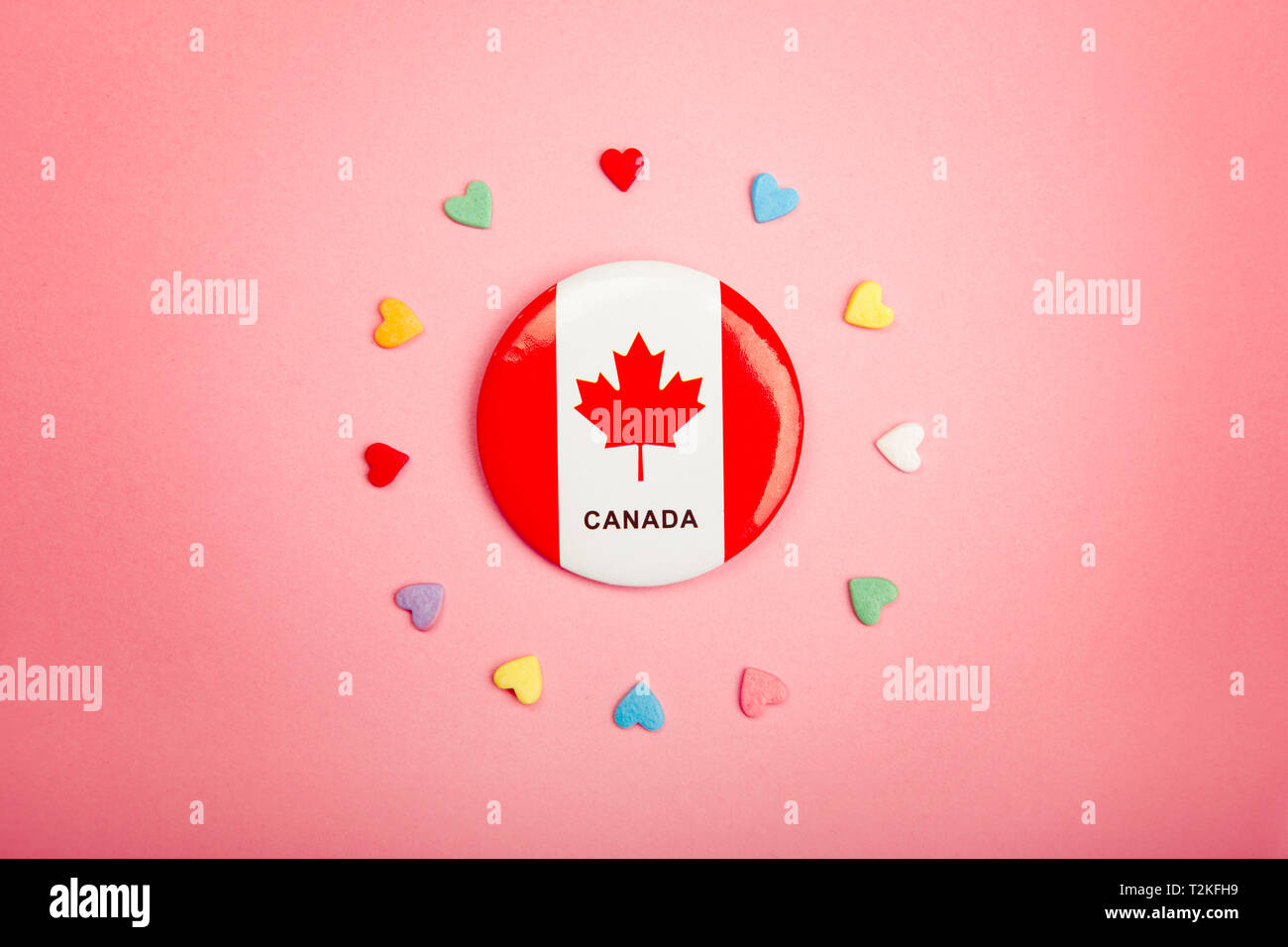 Felice giorno Canada biglietto di auguri con la bandiera canadese nel centro medio e molte caramelle colorate cuori attorno ad esso su coralli viventi sfondo rosa. Foto Stock