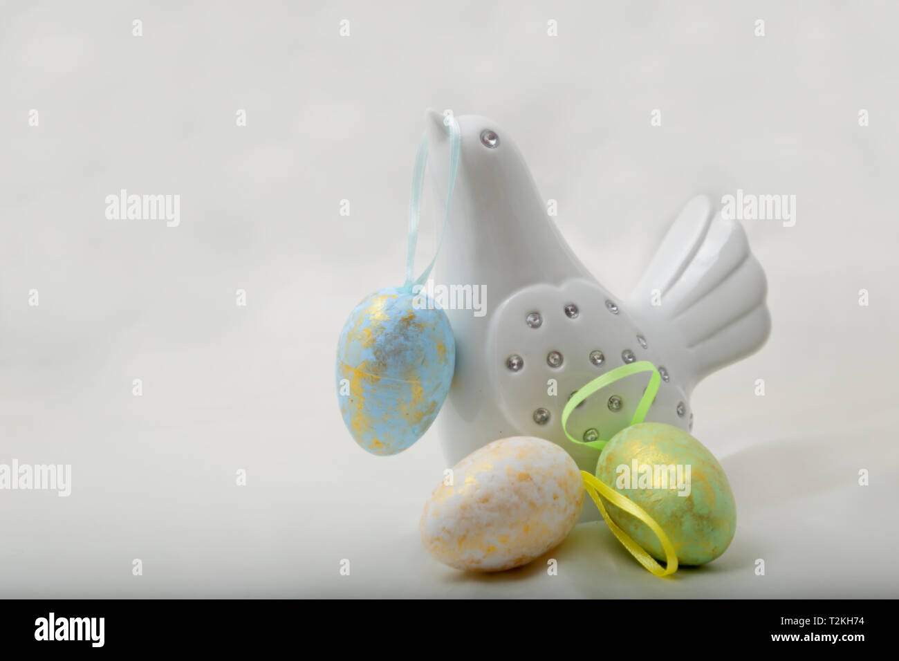 Un bianco uccello decorativo con colorate uova di Pasqua. Uno appeso sul suo becco. Foto Stock