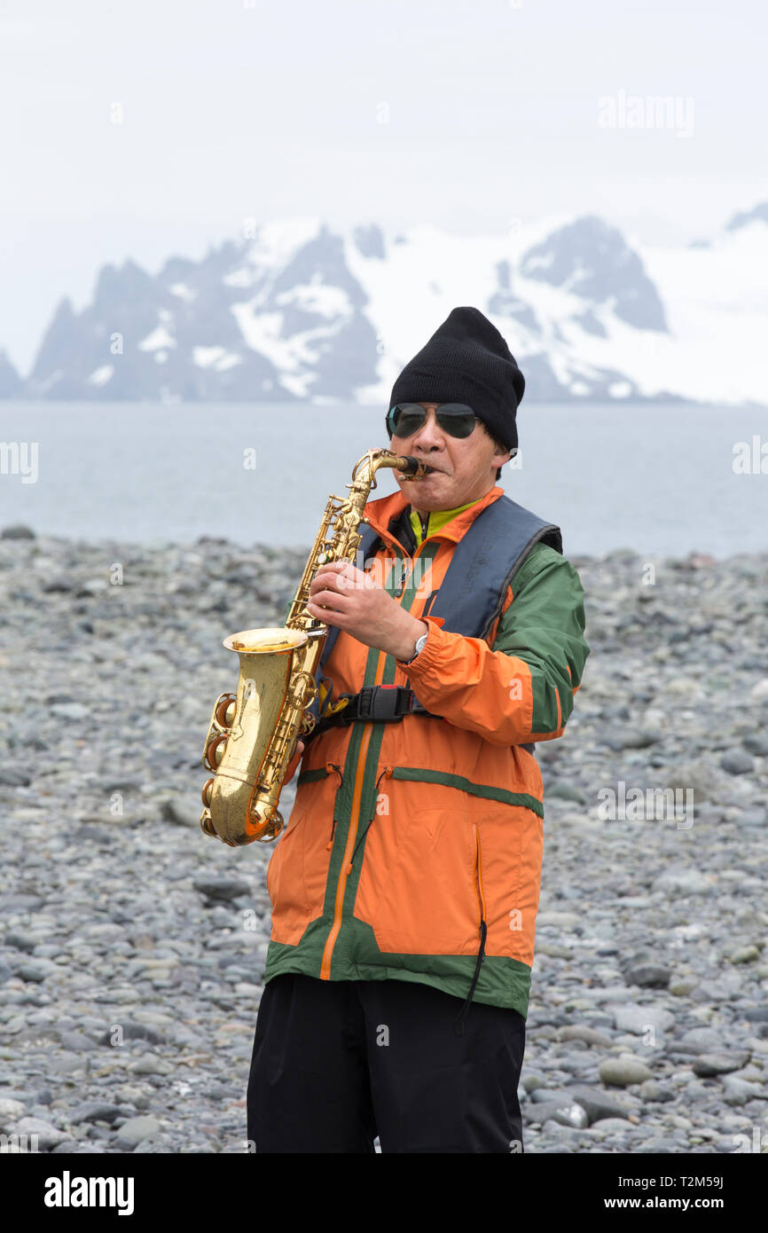 Un sud coreano tourist giocando un sassofono presso Yankee Harbour, Antartico peninsulare. Foto Stock