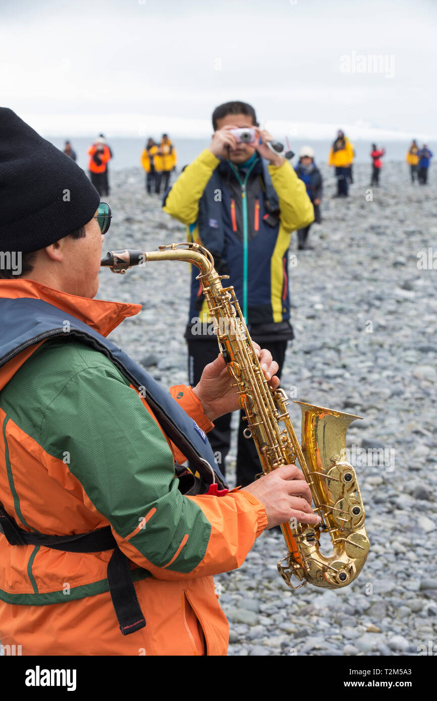 Un sud coreano tourist giocando un sassofono presso Yankee Harbour, Antartico peninsulare. Foto Stock