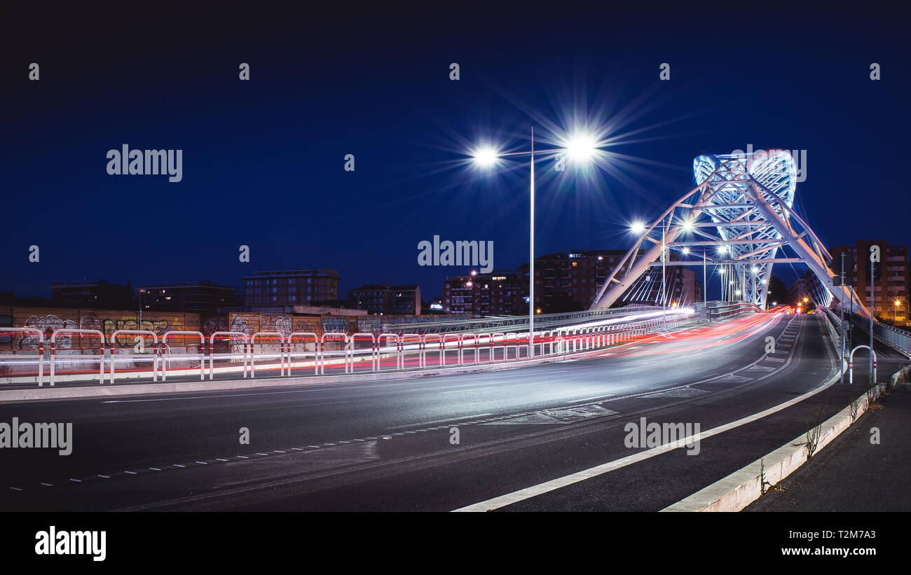 Roma, Italia - 7/31/2019: il moderno ponte bianco dedicato a Settimia Spizzichino, di notte, con i sentieri della luce dei fari di automobile e la str Foto Stock