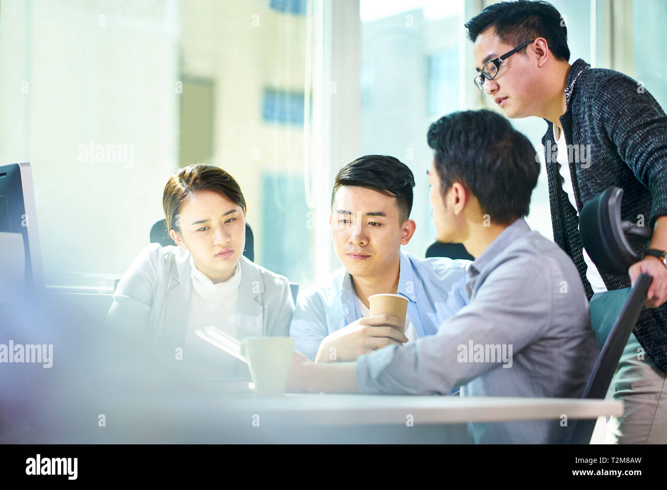 Quattro giovani imprenditori asiatici riuniti a discutere di office business plan utilizzando tablet PC. Foto Stock