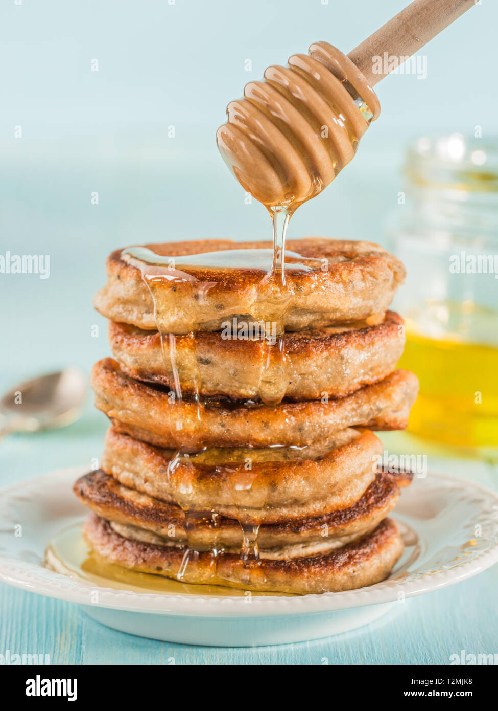 Pila di piccole pancake con banana e semi di chia nel miele su fondo azzurro.  Il
