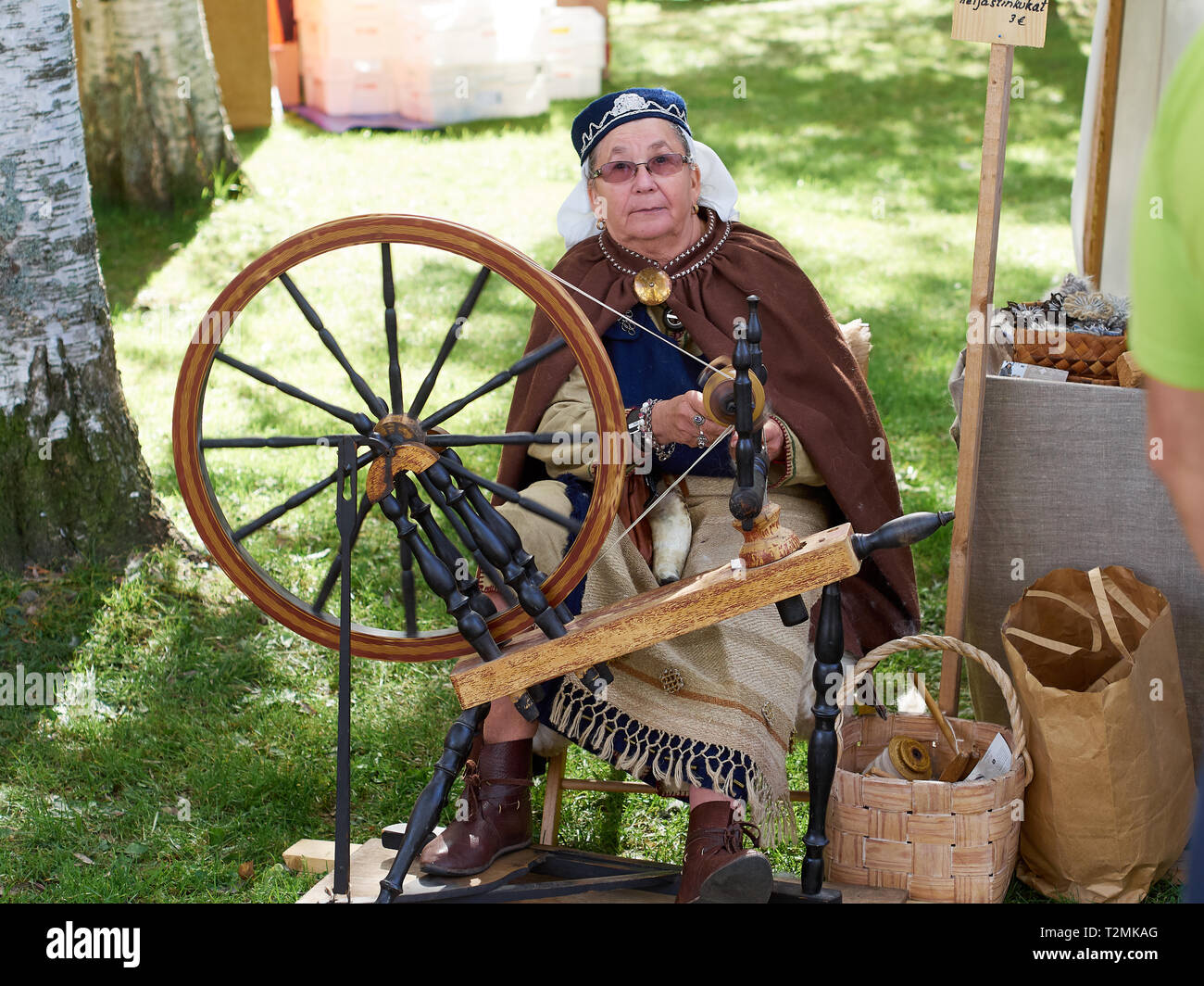 Hämeenlinna, Finlandia - Agosto 17, 2014: donna anziana creazione sbadiglio con una vecchia ruota di filatura al festival medievale su una soleggiata giornata estiva. Foto Stock