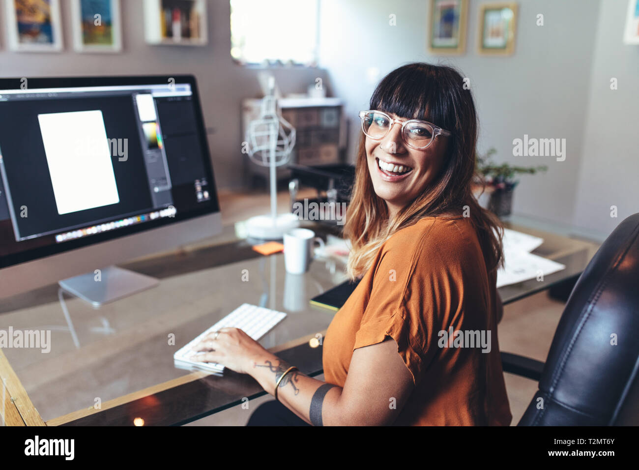 In prossimità di una donna sorridente seduto alla sua scrivania in ufficio con un computer di fronte. Vista laterale di un allegro imprenditrice in ufficio a lavorare sul compute Foto Stock