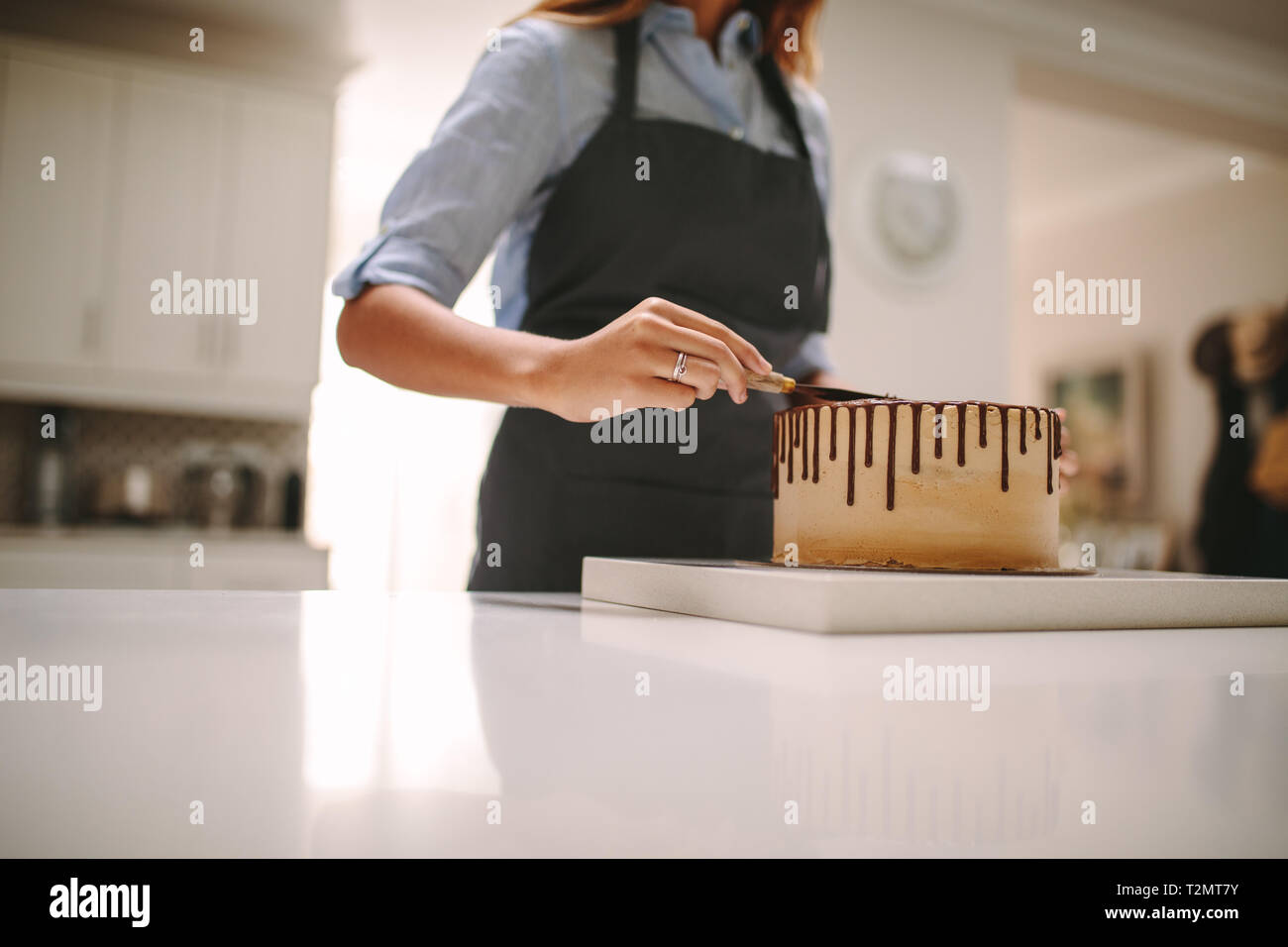 Ritagliato colpo di femmine nel grembiule preparare una torta al cioccolato in cucina. Lo chef donna applicando la glassa di torta. Foto Stock