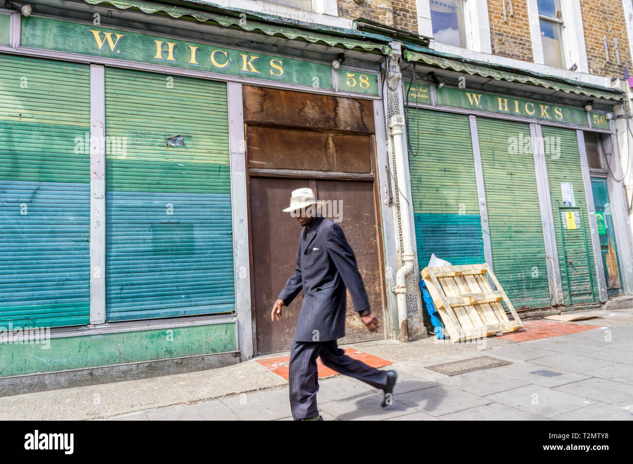 L'uomo (motion sfocata) a piedi nella parte anteriore del negozio chiuso in Golborne Road, Notting Hill. Foto Stock