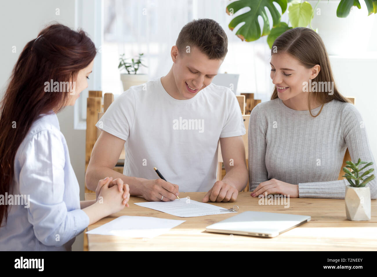 Tre giovani popolo millenario seduto alla scrivania in ufficio agenzia. Famiglia sposato giovane sorridenti firmare un contratto il documento cartaceo. Spostare spostare Foto Stock