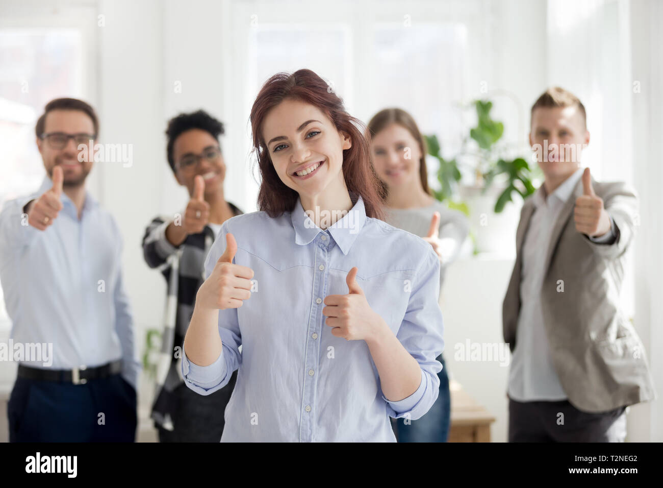 Felice ragazza con gruppo di multirazziale millenario imprenditori positivo su sfondo permanente insieme sorridente in ufficio con le dita fino alla ricerca di ca Foto Stock