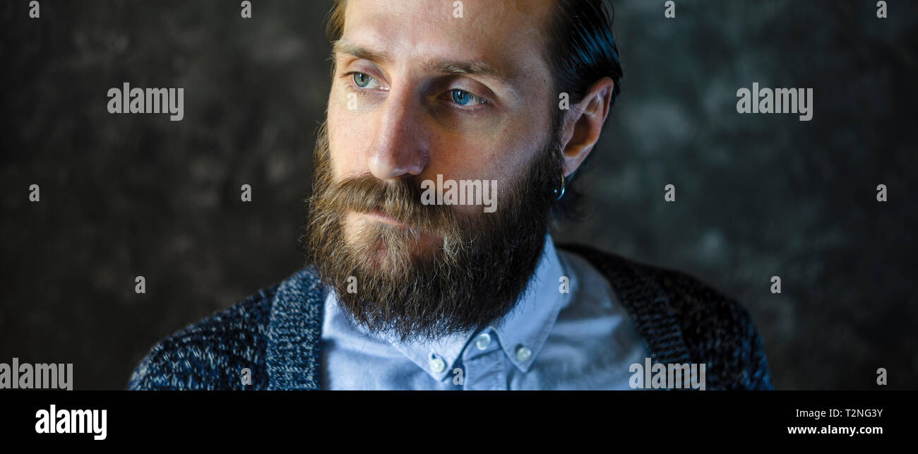 Ritratto di moda di un pensieroso uomo barbuto in una camicia blu e blu cardigan lavorato a maglia su sfondo grigio. Riflessività Concept Foto Stock
