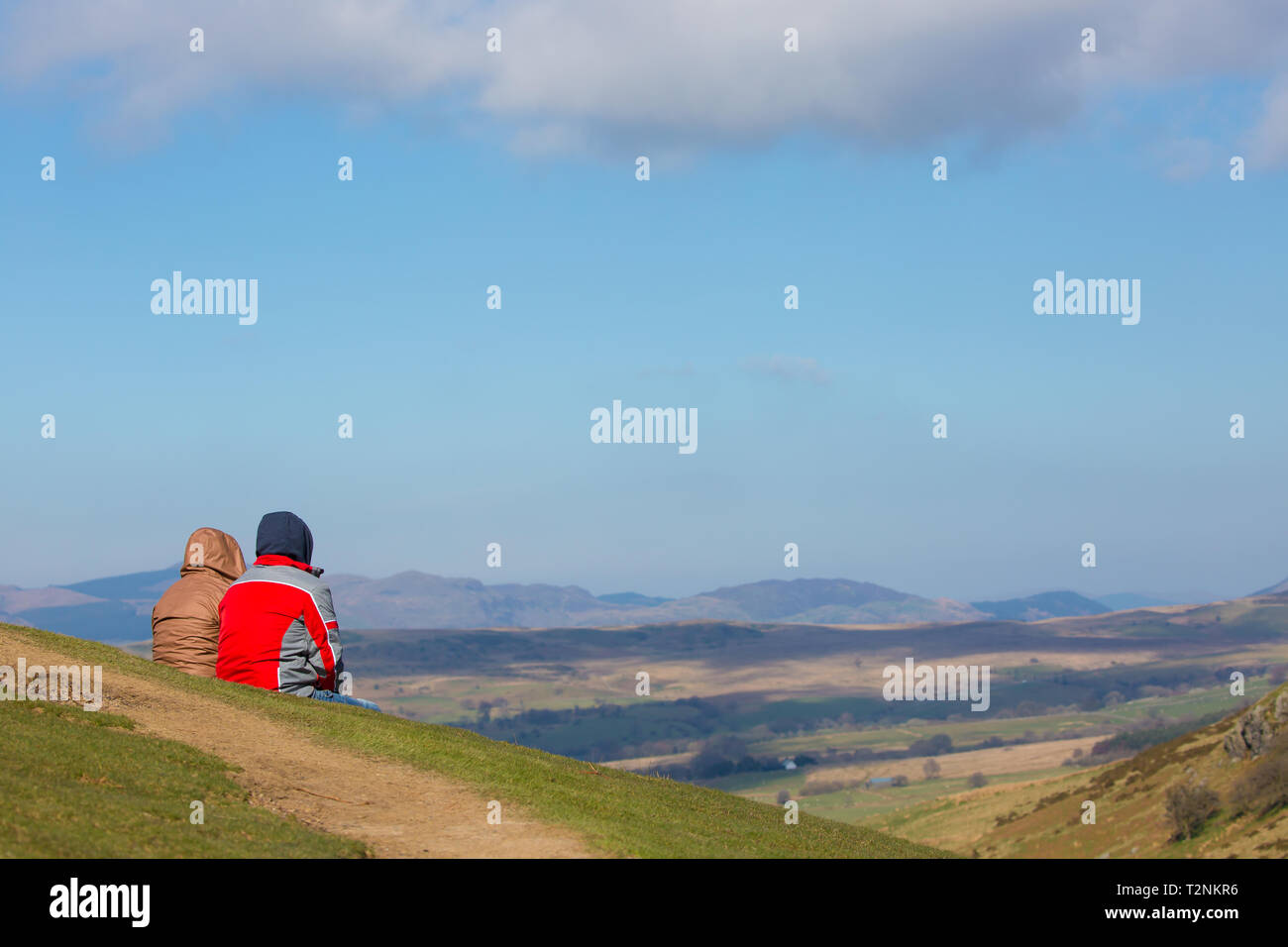 Vista posteriore del giovane fino una montagna nel Mid-Wales seduti sul pendio erboso, nella luce del sole, con lo sguardo al paesaggio spettacolare vista di fronte a loro. Foto Stock