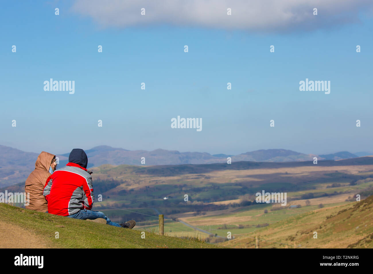 Vista posteriore del giovane fino una montagna nel Mid-Wales seduti insieme sul pendio erboso nella luce del sole, con lo sguardo al paesaggio spettacolare vista di fronte a loro. Foto Stock