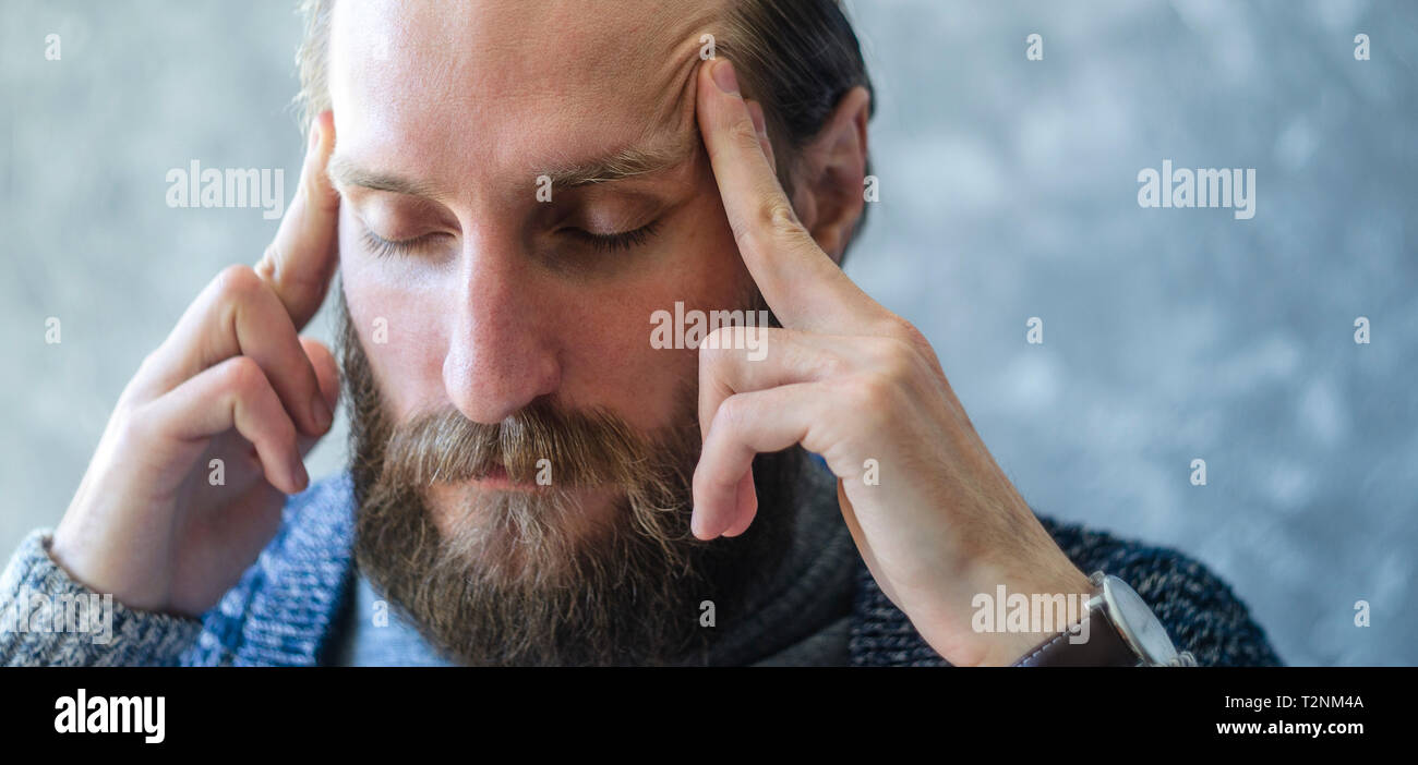 Stanco di un giovane uomo con la barba massaggi i suoi Templi con le sue dita. Pensieroso stato meditativo Concept Foto Stock