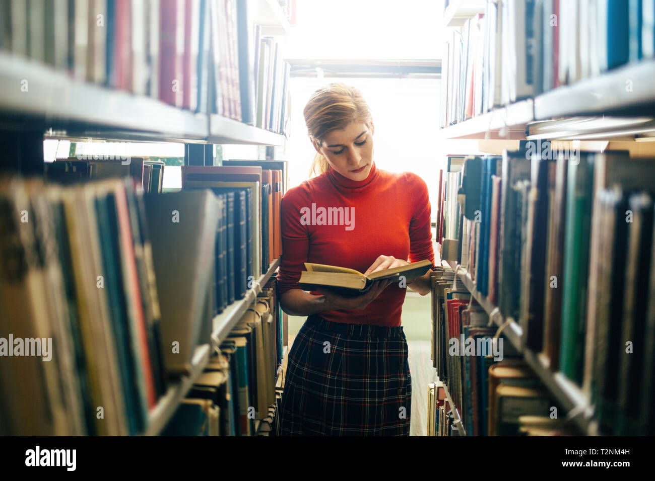 Giovani attraenti bibliotecario leggendo un libro tra gli scaffali della libreria Foto Stock