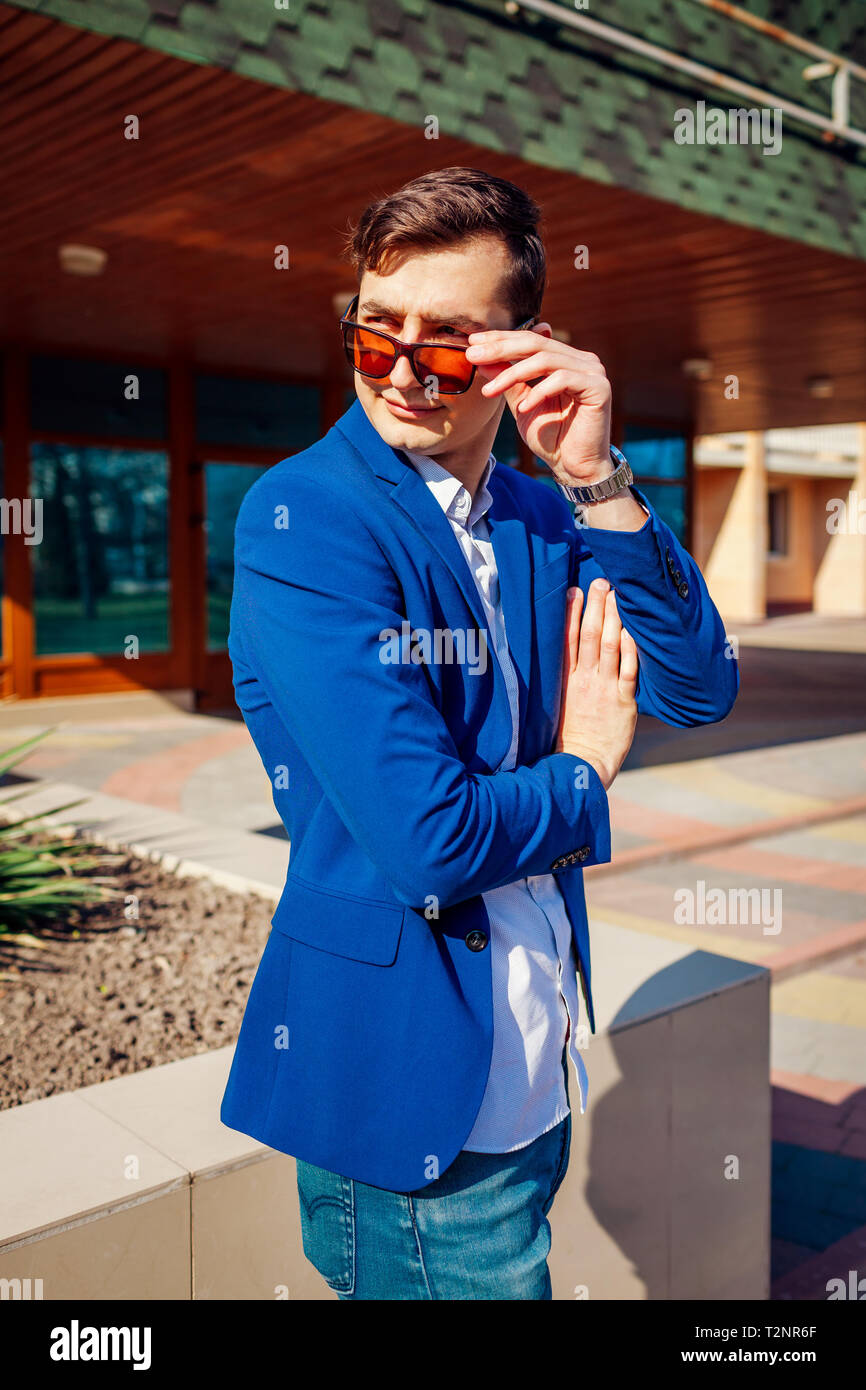 Felice giovane elegante uomo a camminare in città. Bel ragazzo indossa abiti classici e accessori e togliere i bicchieri. Spring street fashion. Foto Stock