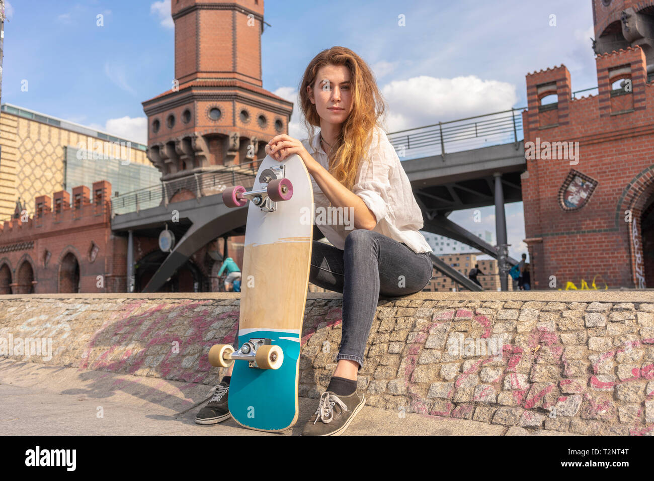 Giovane donna con lo skateboard in appoggio sul ponte Oberbaum nella città di Berlino, Germania Foto Stock