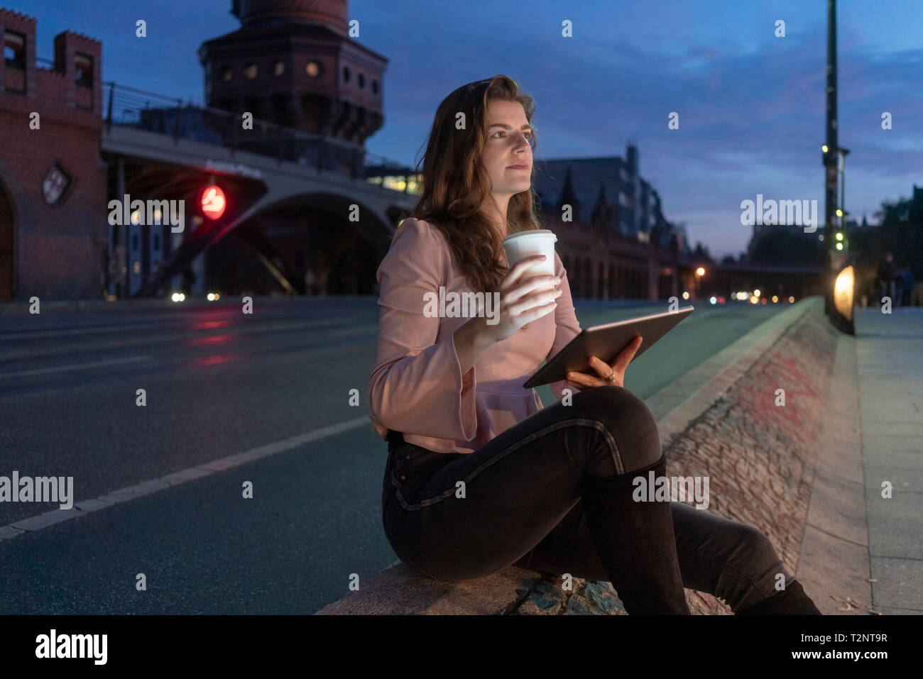 Giovane donna holding bevanda calda e con tavoletta digitale sul ponte, Berlino, Germania Foto Stock