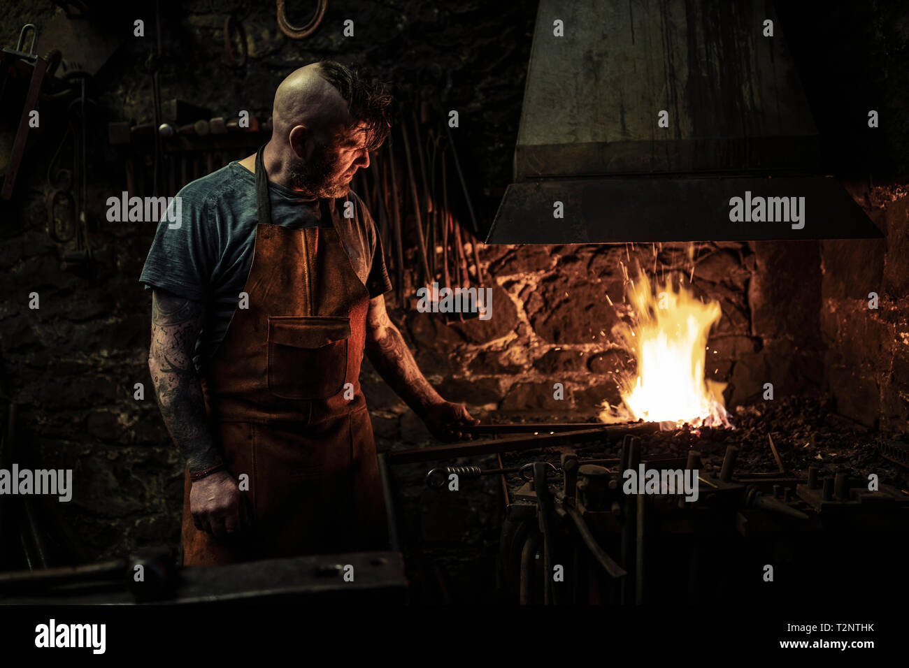 Maschio maturo fabbro riscaldamento metallico sul fuoco aperto in officina Foto Stock