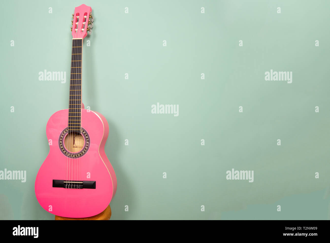 Chitarra rosa davanti a uno sfondo verde. Con lo spazio aggiuntivo sulla destra si può mettere il proprio testo Foto Stock