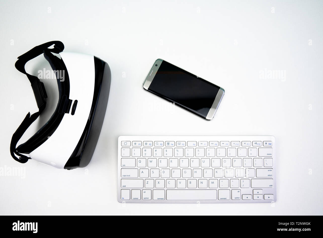 Vista dall'alto di differenti tecnologie wireless su uno sfondo bianco. Una realtà virtuale auricolare, controller di gioco, tastiera e uno smartphone Foto Stock