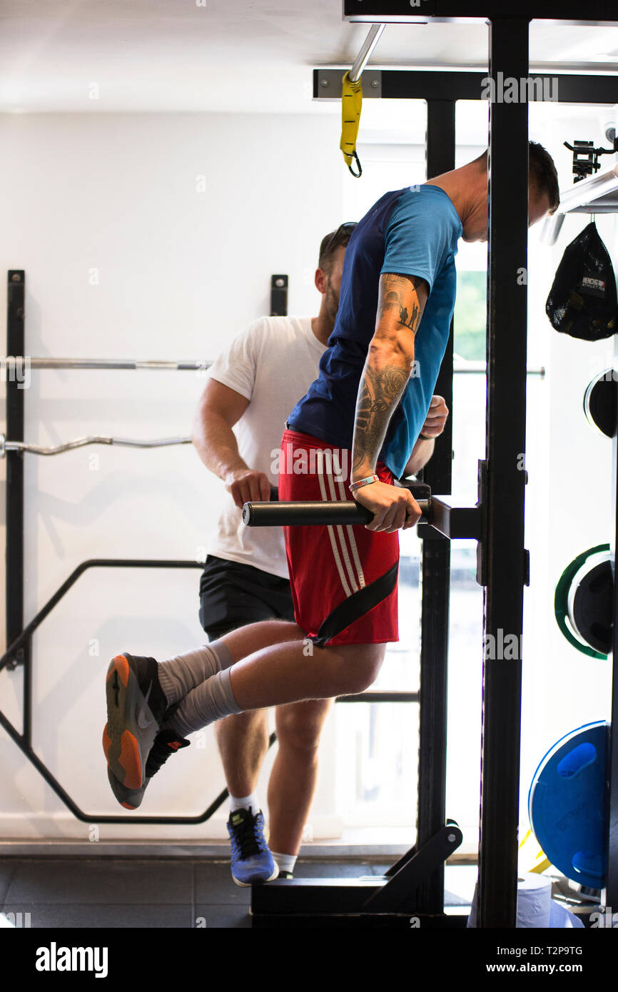Maschio di Personal Trainer training di un client maschio sul rack peso facendo bicipite salse Foto Stock