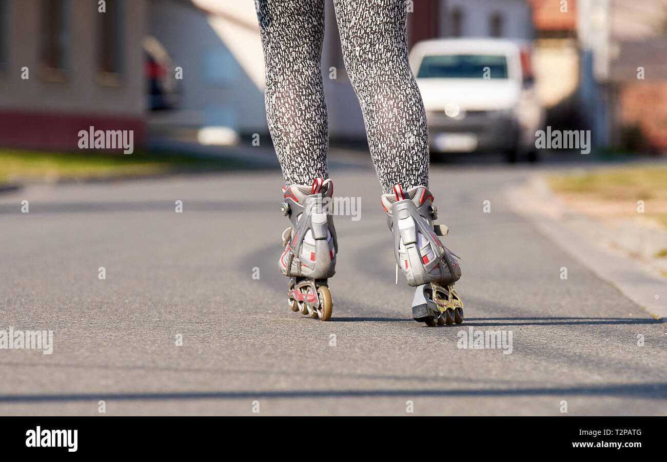Gambe femmina con inline pattini a rotelle. Strada asfaltata in città con le automobili e gli edifici. Foto Stock