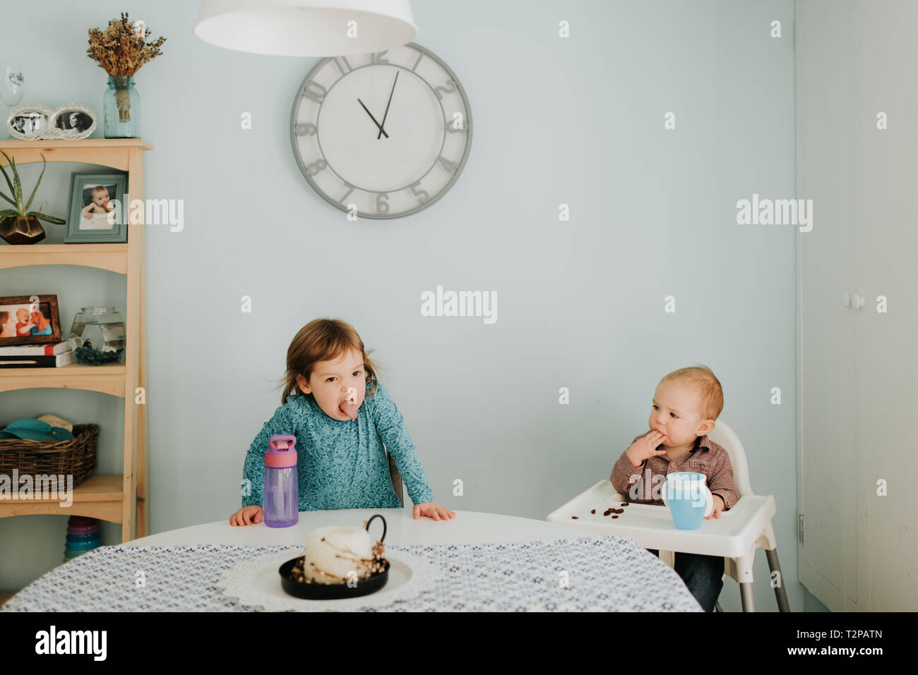 Toddler femmina a tavola e baby fratello in sedia alta Foto Stock