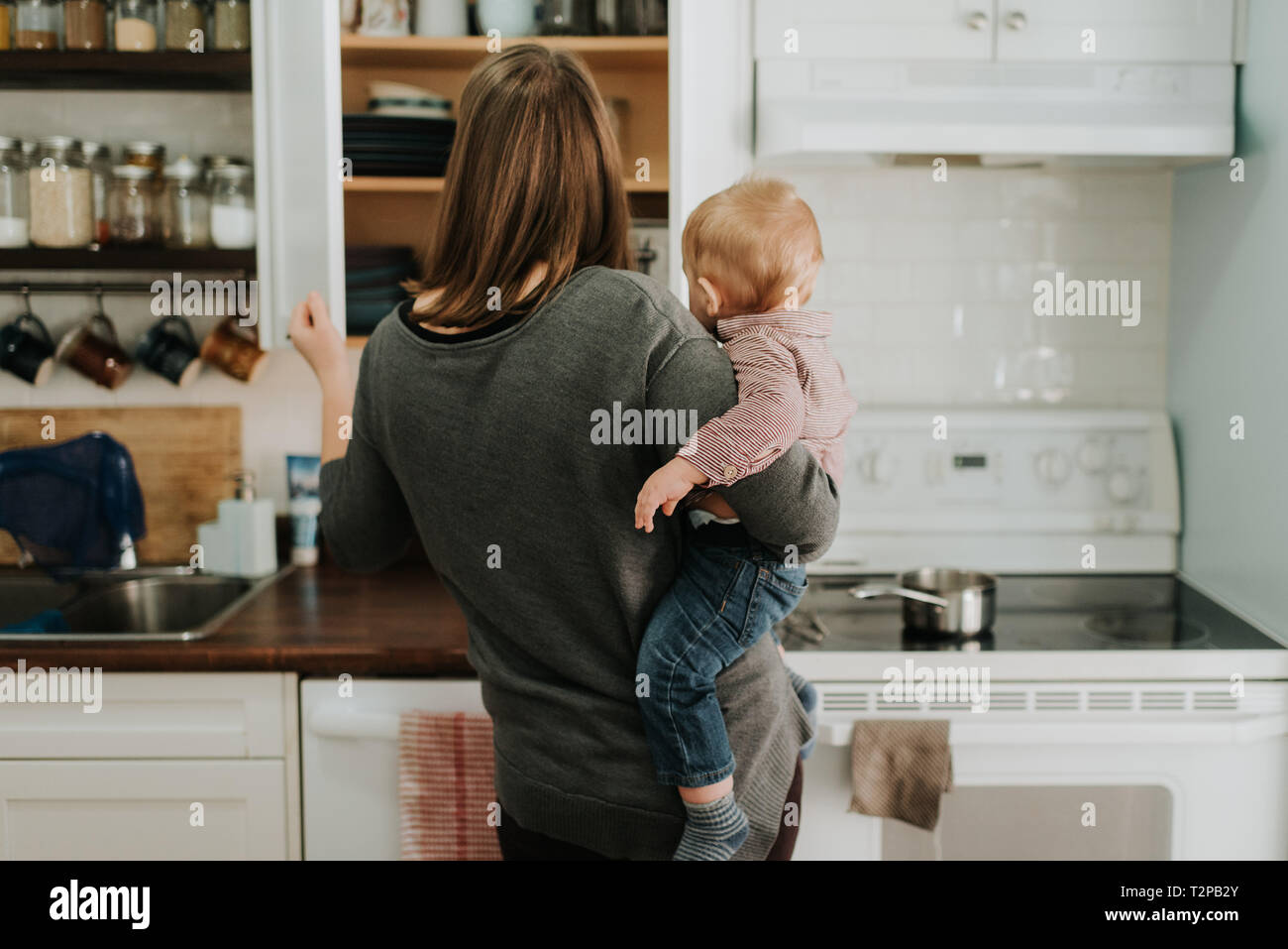 Madre bambino portando figlio di preparare alimenti in cucina, vista posteriore Foto Stock