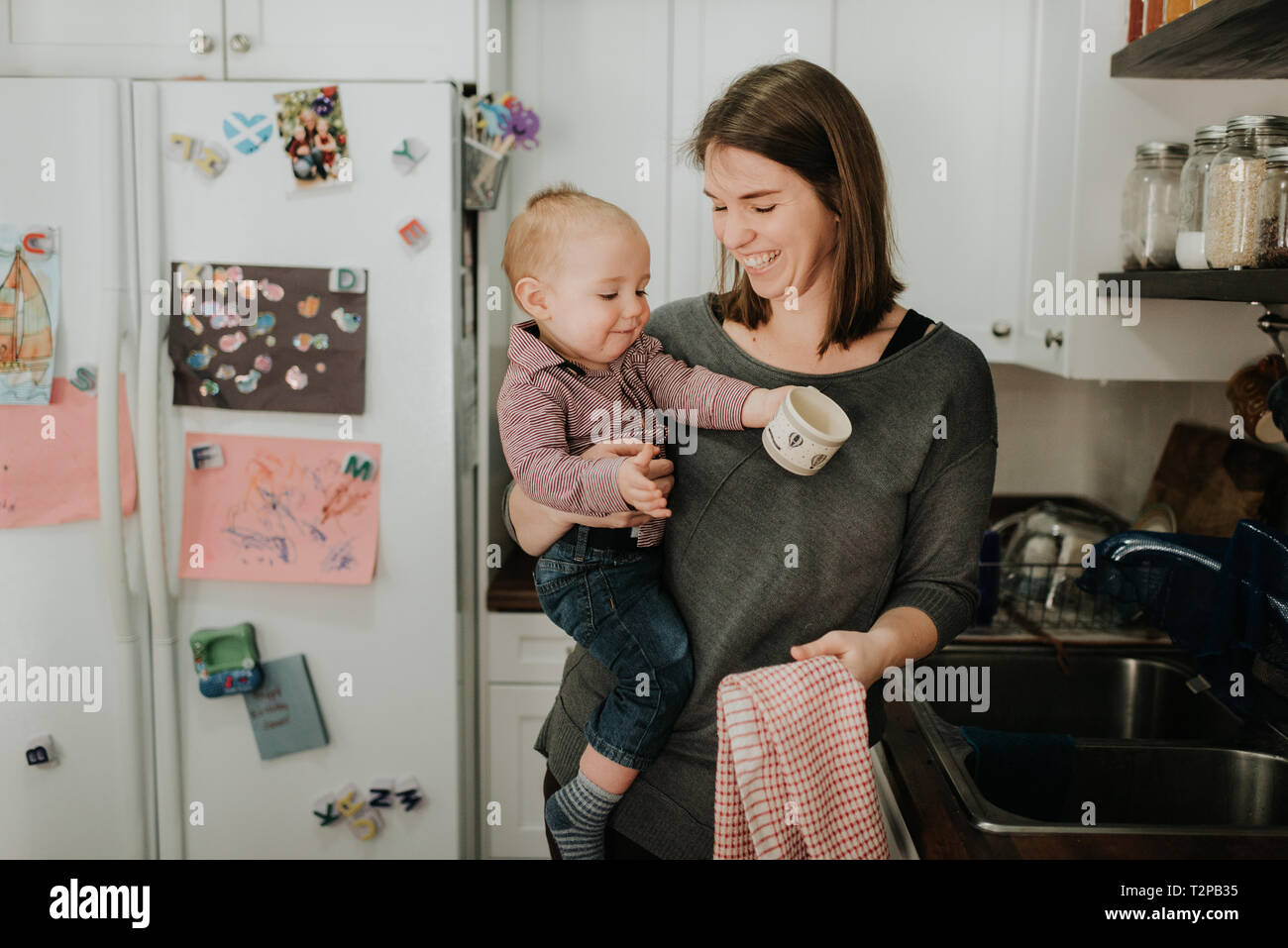 Madre bambino portando figlio piatti di essiccazione in cucina Foto Stock