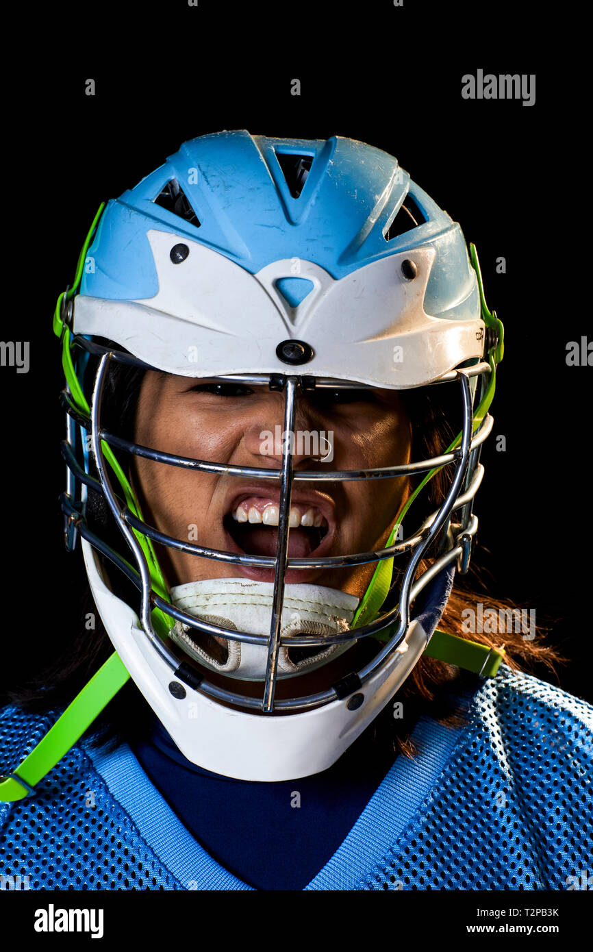 Giovane maschio lacrosse player in lacrosse Casco gridando, close up ritratto su sfondo nero Foto Stock