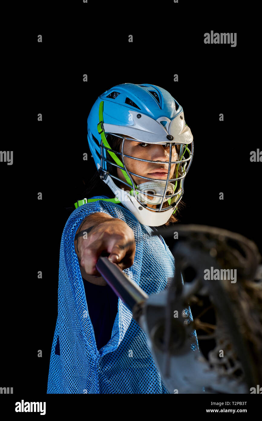 Giovane maschio lacrosse player affondo con lacrosse stick, ritratto su sfondo nero Foto Stock