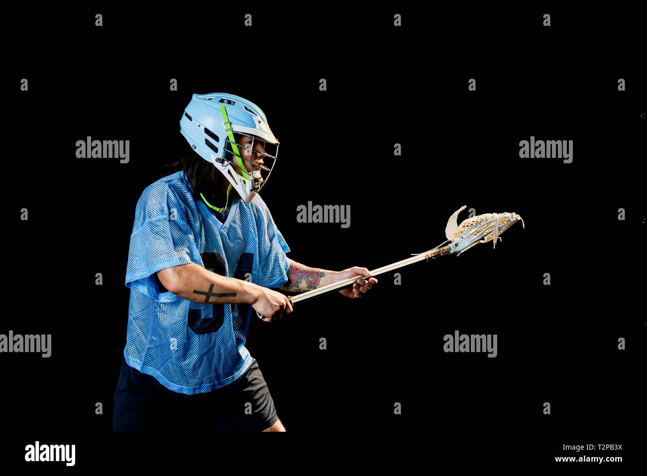 Giovane maschio lacrosse player in bilico con lacrosse stick, su sfondo nero Foto Stock