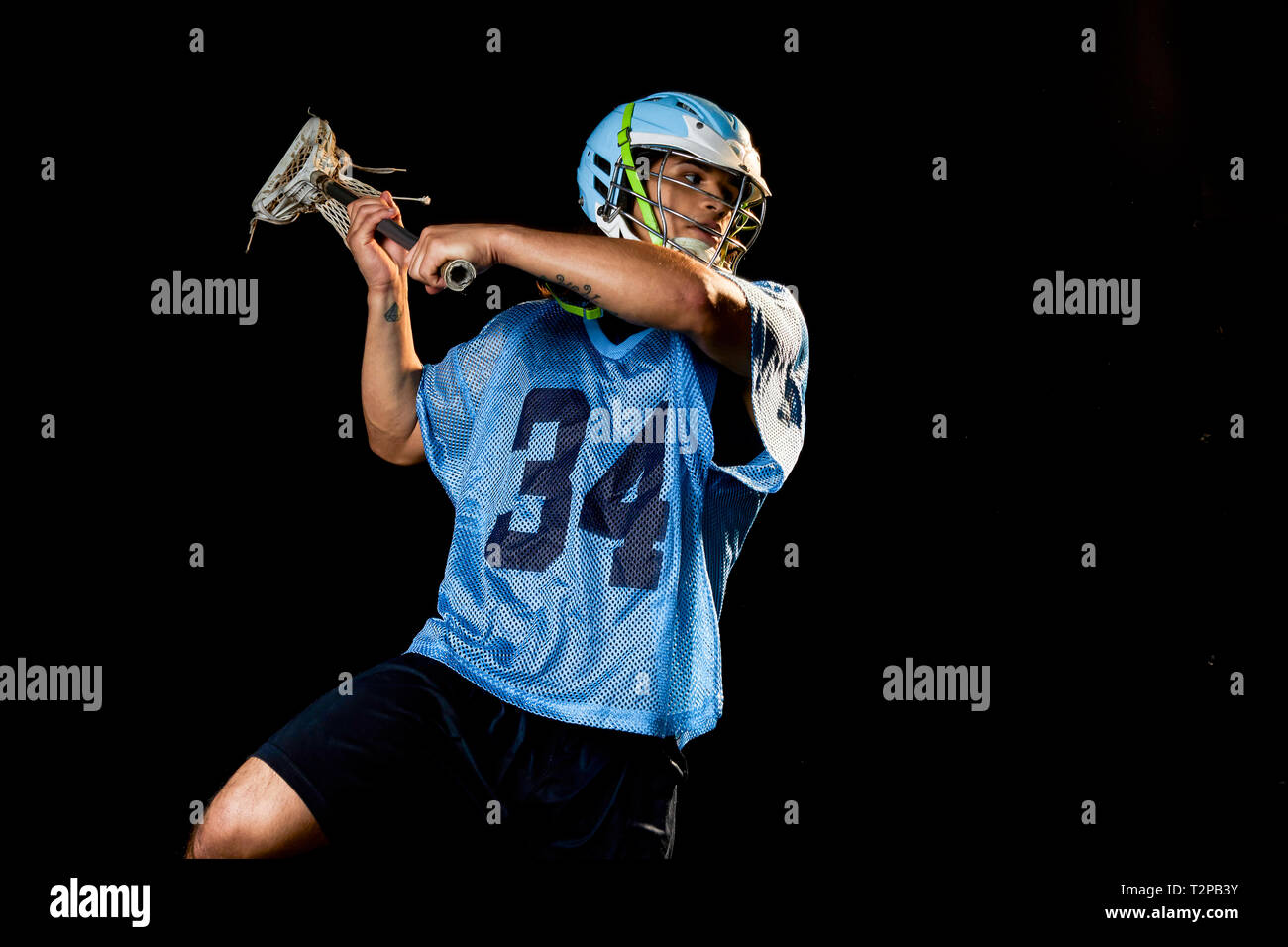 Giovane maschio lacrosse player in azione con lacrosse stick, su sfondo nero Foto Stock
