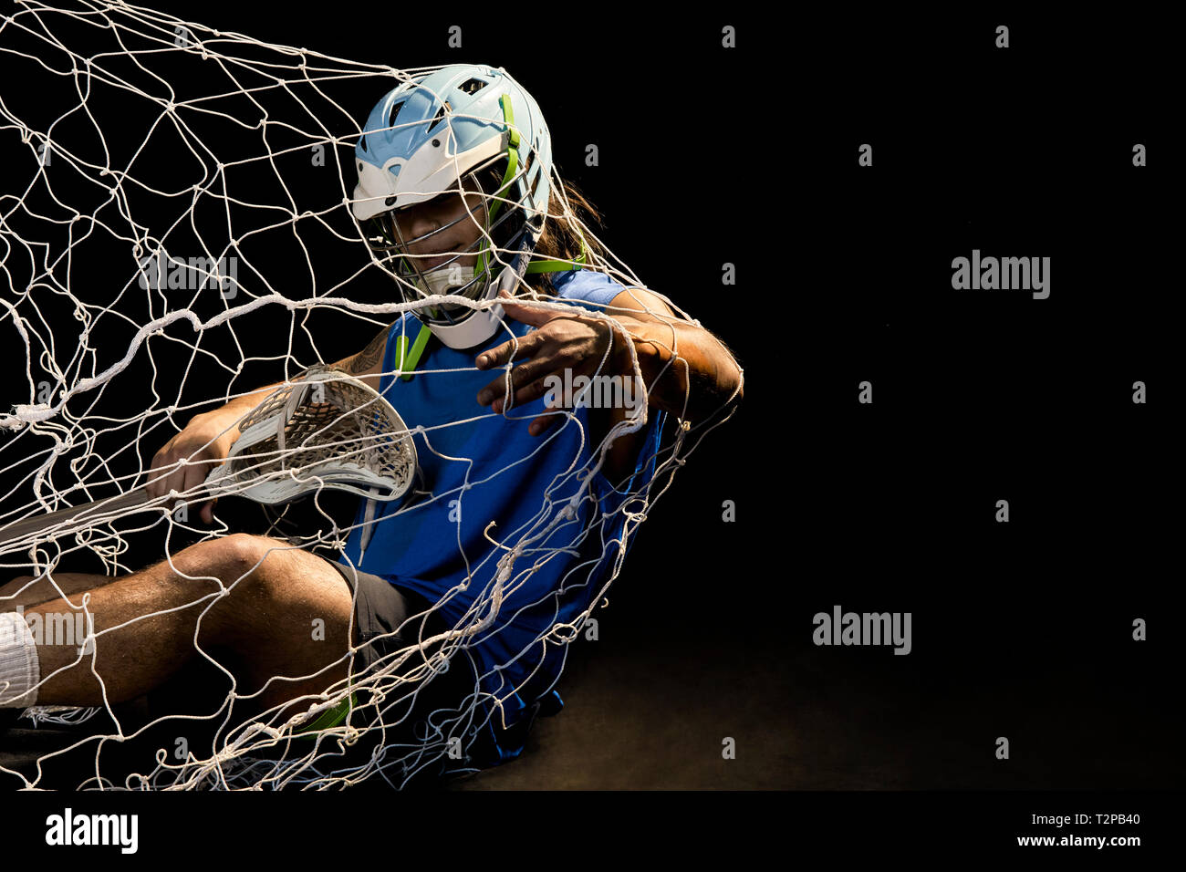 Giovane maschio lacrosse player in azione di cadere nella rete, su sfondo nero Foto Stock