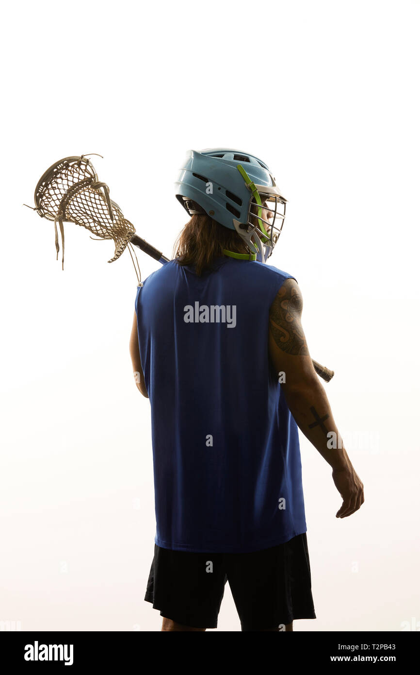 Giovane maschio lacrosse giocatore porta lacrosse stick sulla sua spalla, vista posteriore contro lo sfondo bianco Foto Stock